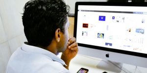 man sitting in front of silver Apple iMac on table